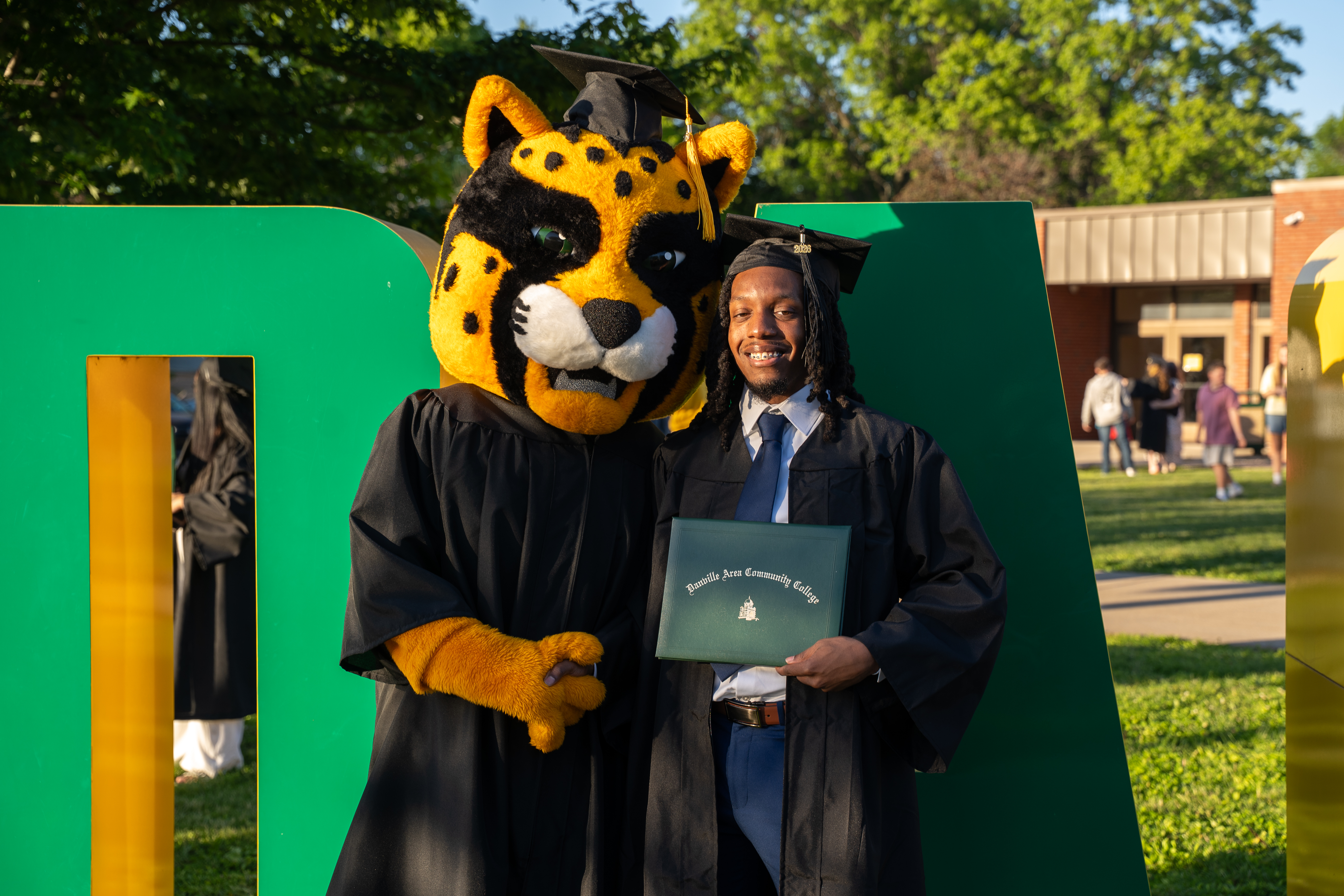 DACC's Mascot Mick Jaguar with a graduating student in a cap and gown